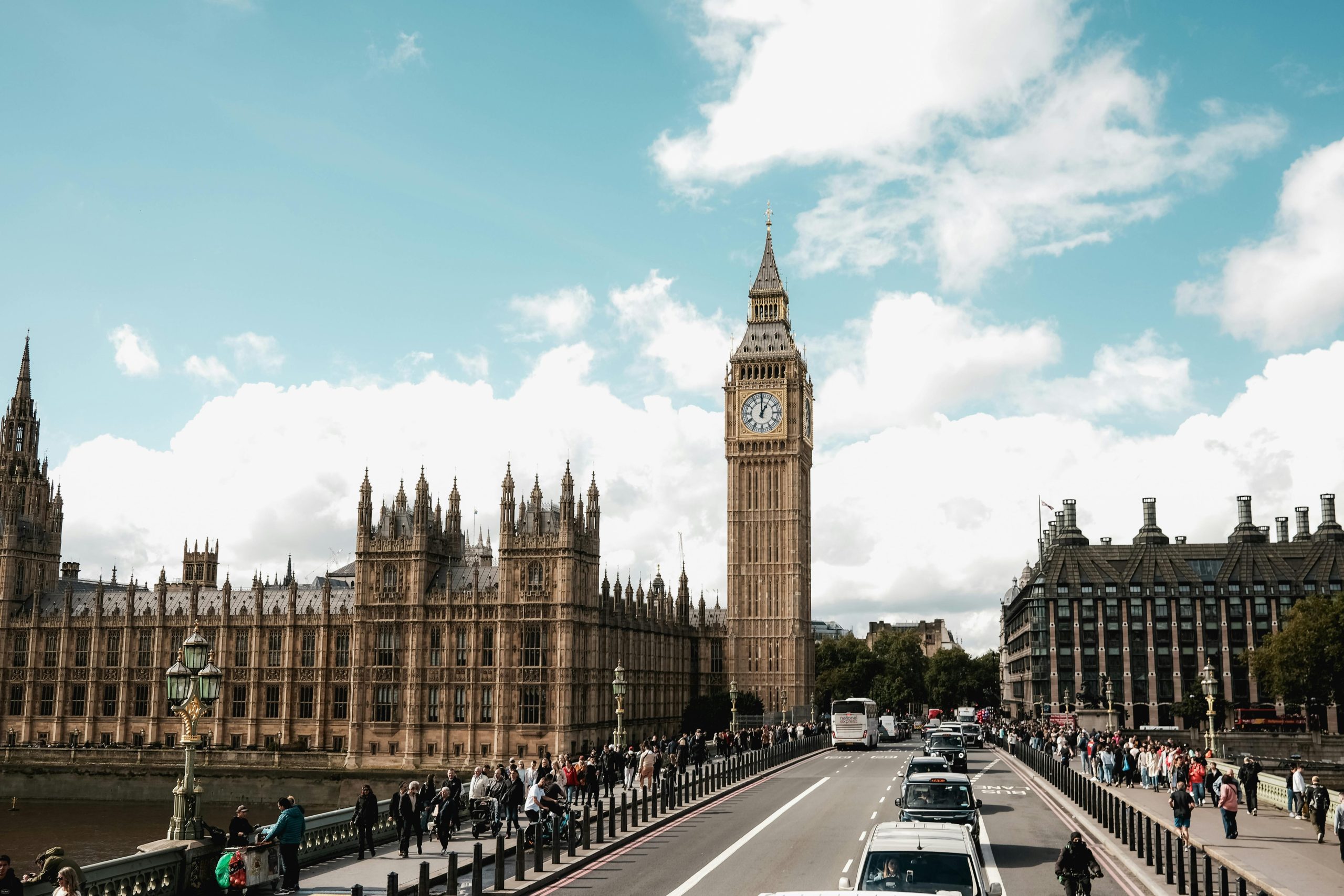 The iconic Big Ben and Westminster Bridge with bustling pedestrians and traffic under a bright sky.